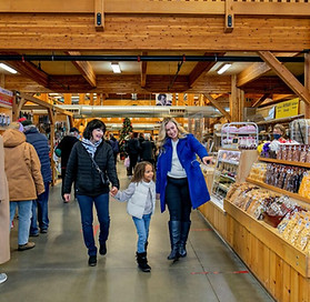 Two women holding hands with a small girl while pointing out sweet treats inside the market building 