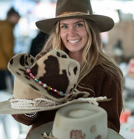 A woman standing outside St. Jacobs Farmers' Market holding several cowboy hats 