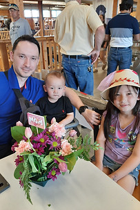 Image of a father and two kids at St. Jacobs Market attending the Mother's Day Workshop and making a floral arrangement thier mom and smiling for the camera