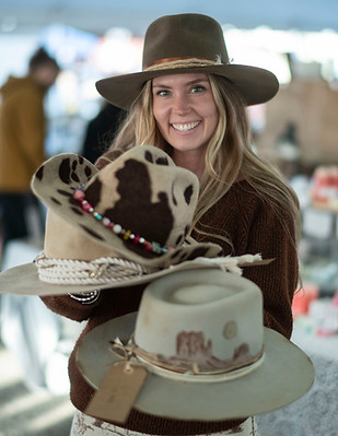 A woman holding several cowboy hats standing in the outdoor market area of St. Jacobs Farmers' Market 