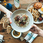 a plate of Jamaican chicken roti over rice being passed overtop of a table filled with delicious foods by Roti Queen
