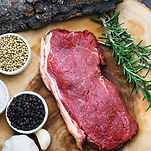A wood platter with a steak, a few sprigs of rosemary and bowls of peppercorn lay on the side by Cloverleaf Farms 