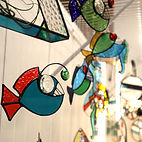 A display of colourful glass art pieces hanging including several fish from Open Green Art Glass