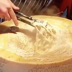 Someone tossing fresh fettuccini in a large parmesan wheel at Busy Cheesy Wheel