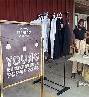 A young women standing behind her table beside a sign reading Young  Entrepreneur Pop-up Zone